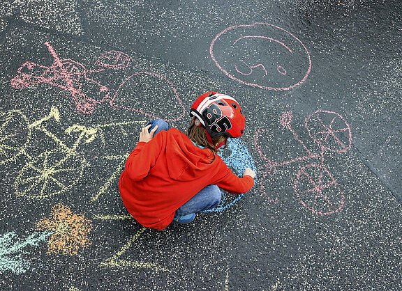 Kind hat Fahrradhelm auf und mal mit Kreide auf die Straße bei der Kidical Mess