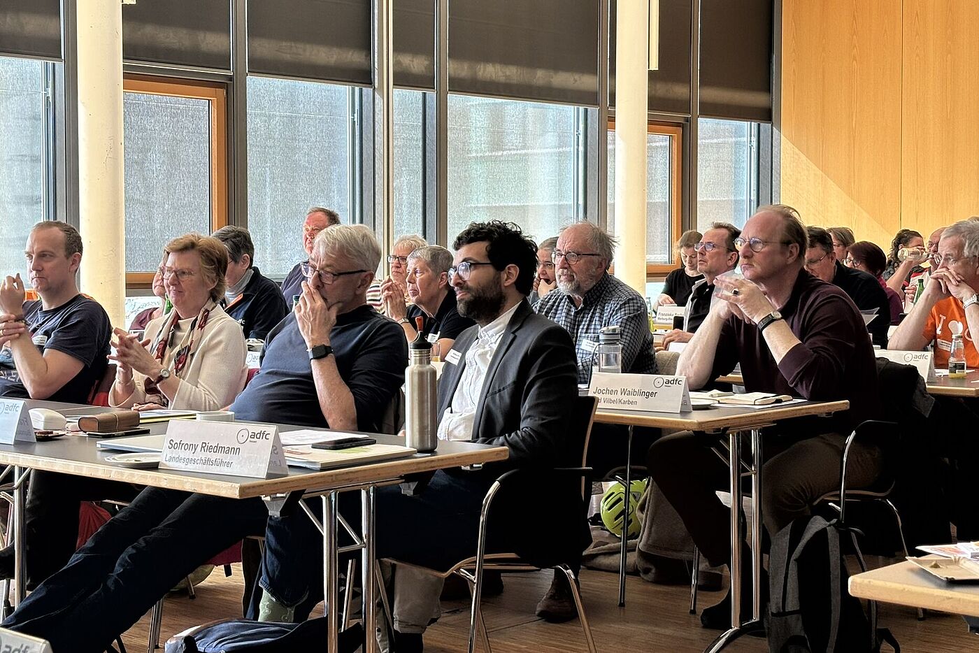 Mehrere Personen sitzen im Plenum nebeneinander und verfolgen den Vortrag