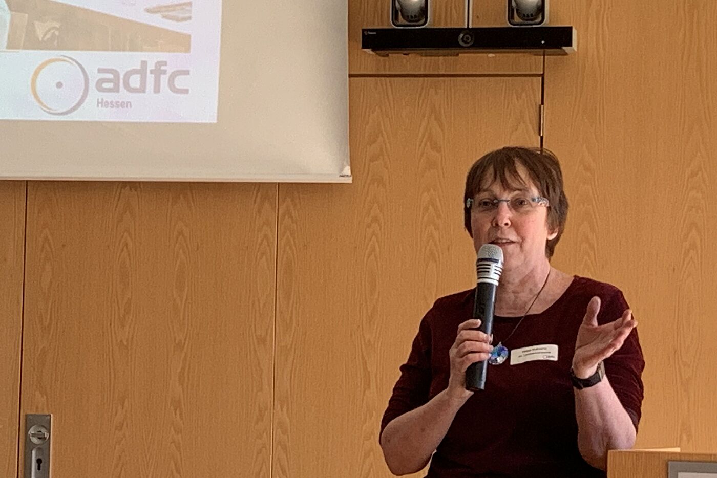 Eine Frau mit einem Mikrofon in der Hand steht vor einer Präsentation
